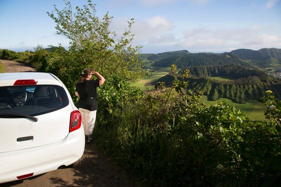 Ein Frau steht neben einem Mietwagen und blickt auf die Landschaft der Azoren