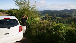 Ein Frau steht neben einem Mietwagen und blickt auf die Landschaft der Azoren