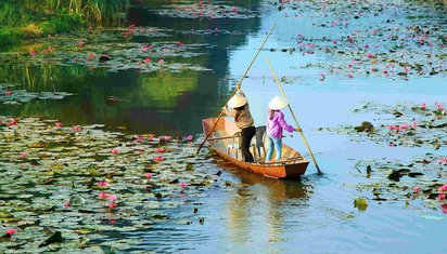 Zwei Frauen paddeln mit ihrem Boot über einen Fluss in Vietnam.