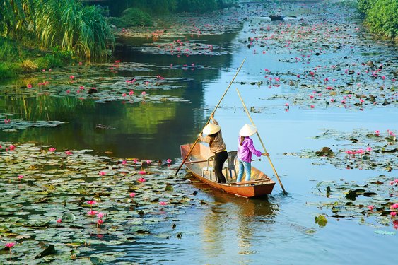 Zwei Frauen paddeln mit ihrem Boot über einen Fluss in Vietnam.