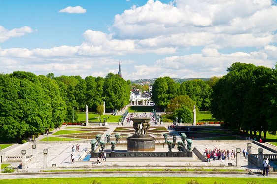 Blick auf einen angelegten Platz im Vigeland-Park mit einem großen Brunnen und Blumenbeeten umstanden von Bäumen.