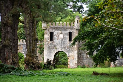 Ein Zinnen-bewehrtes Tor mit anschließender Mauer erhebt sich aus grüner Vegetation.