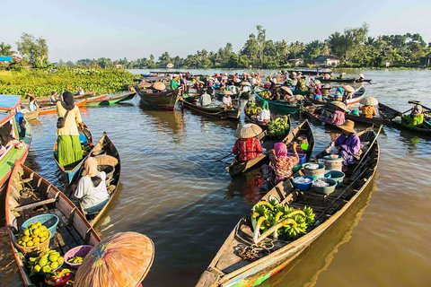 Zahlreiche Boote mit bunt gekleideten Händlerinnen treiben auf einem Fluss. Sie verkaufen frisches Obst, Gemüse und Waren. Viele tragen traditionelle Strohhüte.