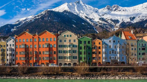 Innsbrucks Architektur Die berühmten bunten Häuser der Innsbrucker Altstadt am Ufer des Inn mit den schneebedeckten Alpen im Hintergrund.