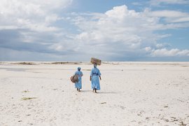Zwei Frauen vom Seaweed Center auf Sansibar gehen entlang eines Strandes.
