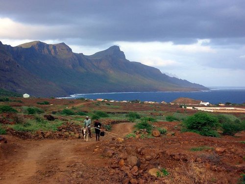 Zwei Männer und ein Esel laufen einen Weg entlang mit dem Meer im Hintergrund auf Sao Nicolau