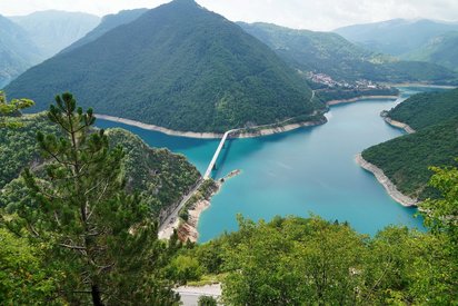 Von einer Anhöhe blickt man steil herunter auf einen blauen, zackig-geformten See, der von bewaldeten Bergen umgeben ist.