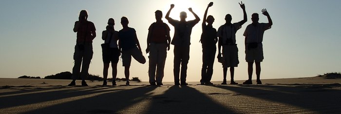Eine Reisegruppe steht bei Sonnenuntergang auf Dünen in Mosambik.