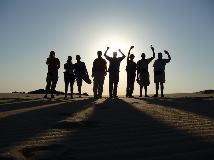 Eine Reisegruppe steht bei Sonnenuntergang auf Dünen in Mosambik.