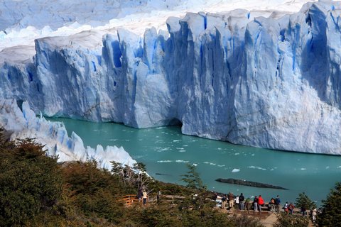 Wandergruppe blickt an einem See auf eine große Gletscherwand