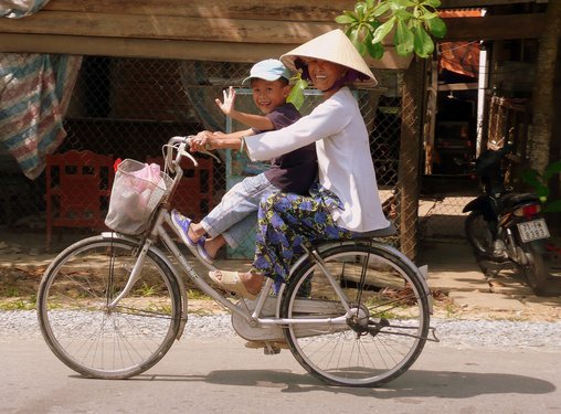 Mutter fährt mit ihrem Kind auf dem Fahrrad in einem Dorf im Mekongdelta.