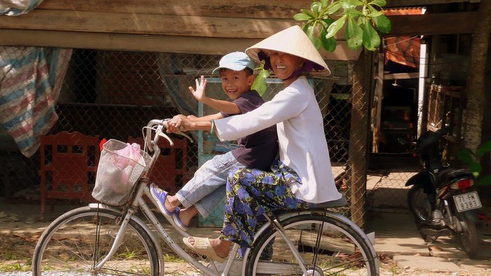 Mutter fährt mit ihrem Kind auf dem Fahrrad in einem Dorf im Mekongdelta.