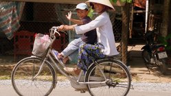 Mutter fährt mit ihrem Kind auf dem Fahrrad in einem Dorf im Mekongdelta.