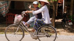 Vietnam – Unterwegs mit dem Fahrrad Mutter fährt mit ihrem Kind auf dem Fahrrad in einem Dorf im Mekongdelta.