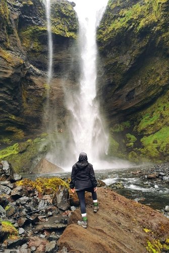 Wanderin am Kvernufoss-Wasserfall in Südisland Eine Person in dunkler Outdoor-Kleidung steht vor dem imposanten Kvernufoss-Wasserfall.