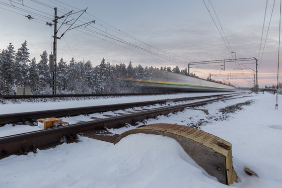 Die Landschaft vorbeiziehen lassen Die Bildmitte wird von Gleisen durchzogen, auf denen eine Zug mit hoher Geschwindigkeit vorüber rauscht. Hinter den Schienen stehen schneebedeckte Bäume, der Bahndamm davor ist ebenfalls schneebedeckt.